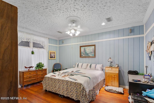 bedroom featuring a textured ceiling, visible vents, ornamental molding, and wood finished floors