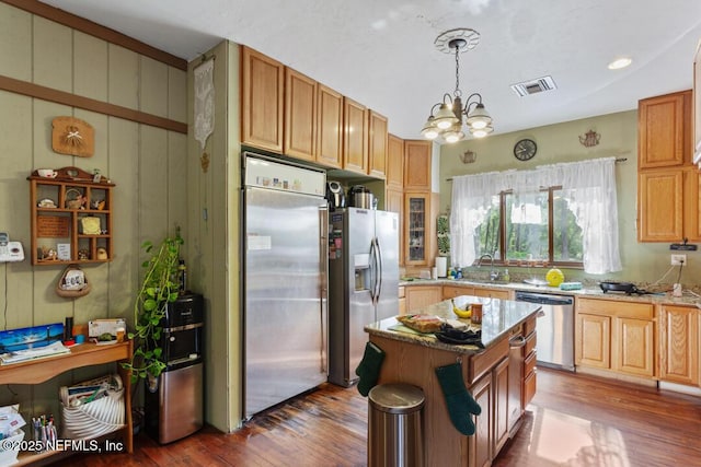 kitchen with light stone countertops, appliances with stainless steel finishes, an inviting chandelier, and wood finished floors