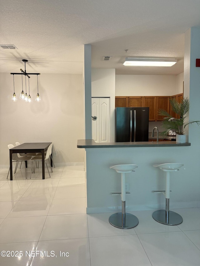 8601 Beach Blvd Unit 711, Jacksonville, FL 32216 - kitchen featuring freestanding refrigerator, brown cabinetry, a peninsula, dark countertops, and tile patterned floors