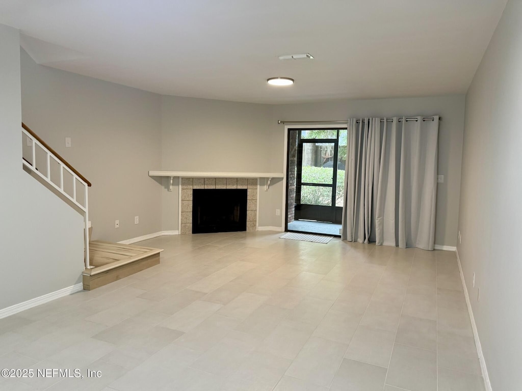 unfurnished living room with baseboards, stairway, and a tile fireplace