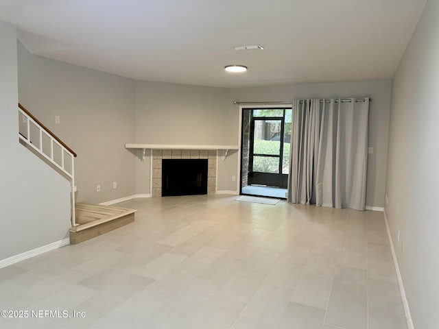 unfurnished living room with baseboards, stairway, and a tile fireplace