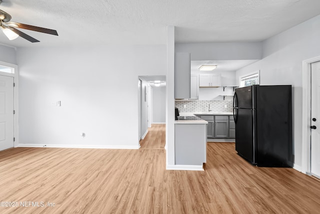 kitchen with freestanding refrigerator, decorative backsplash, ceiling fan, light countertops, and light wood-style flooring