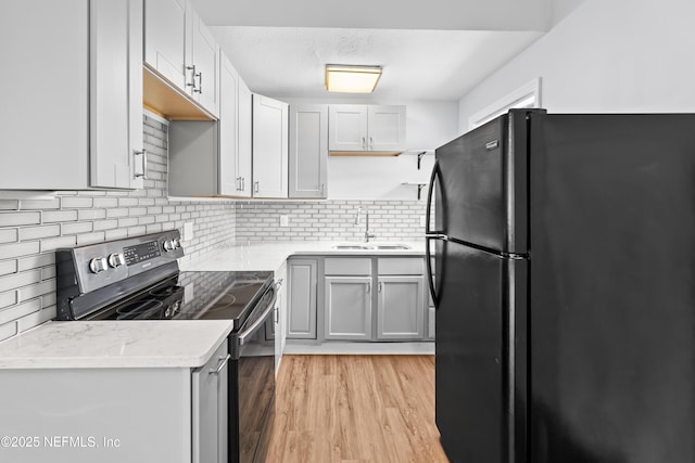 kitchen with decorative backsplash, light wood-type flooring, a sink, freestanding refrigerator, and electric stove