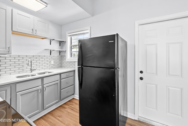 kitchen with a sink, light countertops, decorative backsplash, and freestanding refrigerator