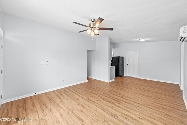 unfurnished living room featuring a ceiling fan, baseboards, light wood-style flooring, and a wall mounted air conditioner