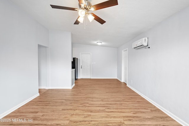 spare room featuring an AC wall unit, a ceiling fan, baseboards, and light wood-style flooring