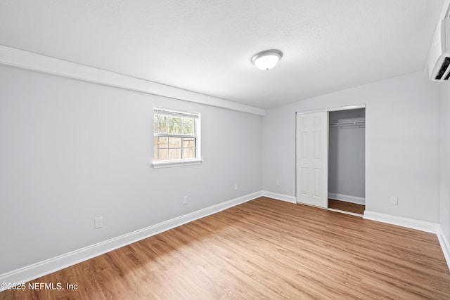 unfurnished bedroom with a closet, baseboards, a wall mounted air conditioner, a textured ceiling, and light wood finished floors