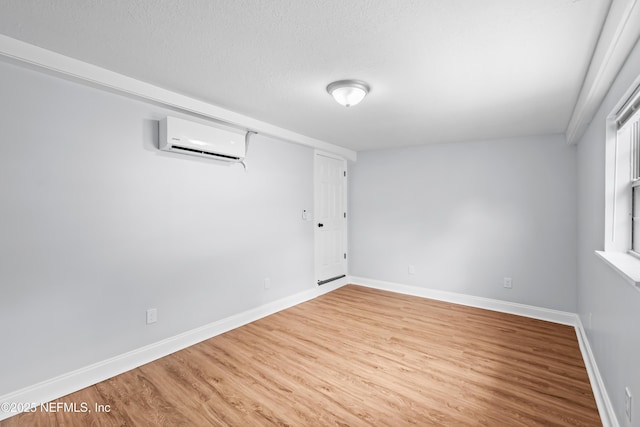 unfurnished room with a textured ceiling, baseboards, a wall mounted AC, and wood finished floors