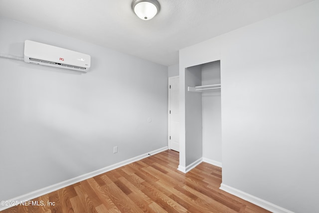 unfurnished bedroom with baseboards, a wall mounted AC, a closet, and wood finished floors