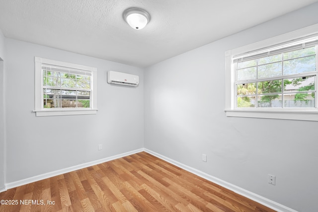 unfurnished room with an AC wall unit, baseboards, light wood finished floors, and a healthy amount of sunlight
