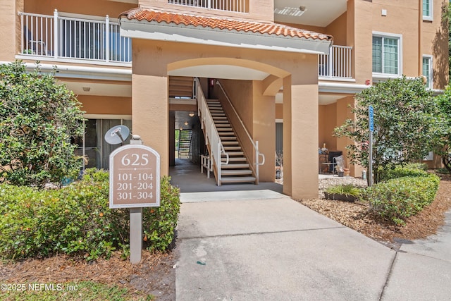 view of exterior entry featuring a balcony, a tile roof, and stucco siding