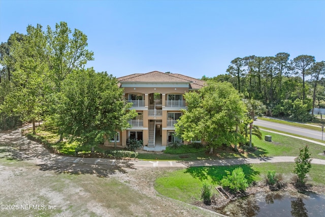 view of front of home with stairs, stucco siding, a front lawn, and a balcony