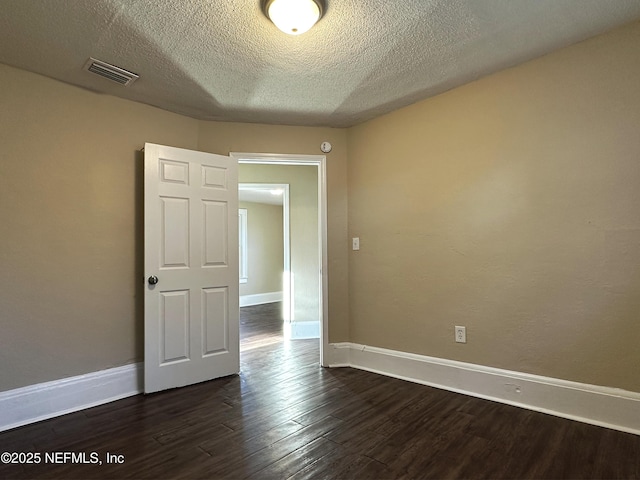 unfurnished room with visible vents, a textured ceiling, dark wood-type flooring, and baseboards