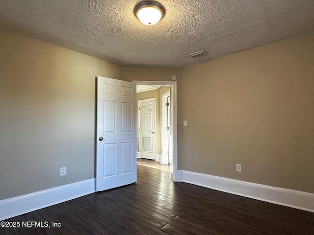 spare room with baseboards, dark wood-style floors, a textured ceiling, and visible vents