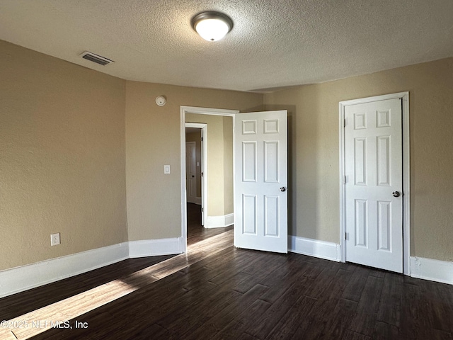 empty room featuring a textured ceiling, visible vents, dark wood-style floors, and baseboards