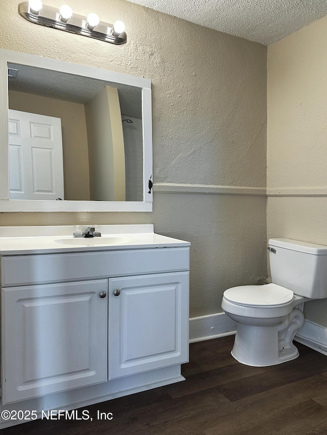 bathroom featuring vanity, a textured wall, wood finished floors, toilet, and baseboards