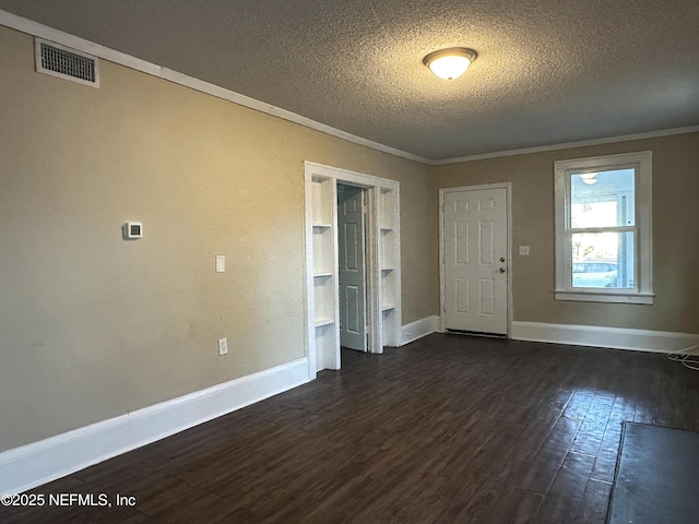 empty room featuring a textured ceiling, dark wood finished floors, baseboards, visible vents, and ornamental molding