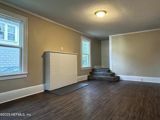 unfurnished living room featuring a textured ceiling, crown molding, dark wood finished floors, baseboards, and stairs