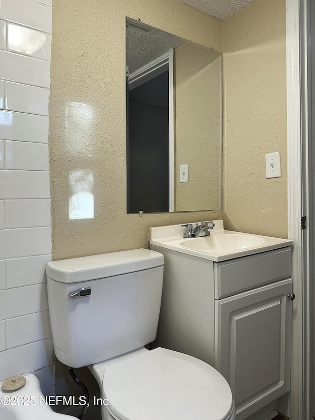 half bathroom featuring vanity, a textured wall, and toilet