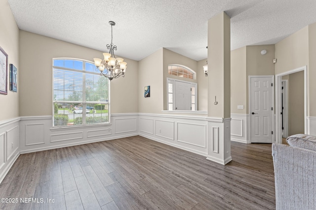 interior space featuring wainscoting, dark wood-style flooring, a textured ceiling, and a chandelier