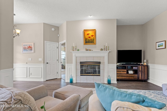 living area featuring a textured ceiling, wainscoting, wood finished floors, and a tile fireplace