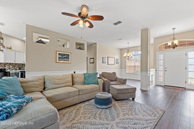 living room with ceiling fan with notable chandelier, wainscoting, dark wood-style flooring, and visible vents