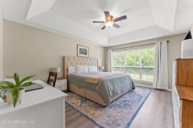 bedroom featuring a textured ceiling, a tray ceiling, a ceiling fan, and light wood finished floors