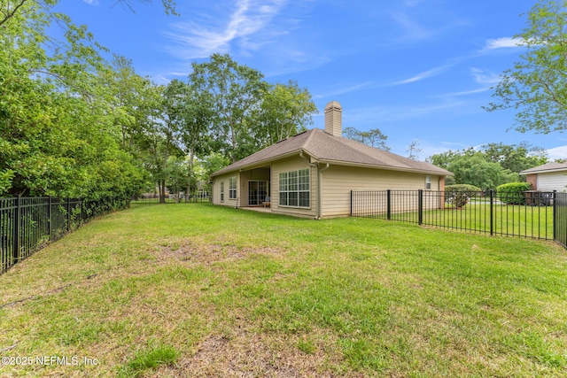 rear view of house with a fenced backyard, a chimney, and a lawn