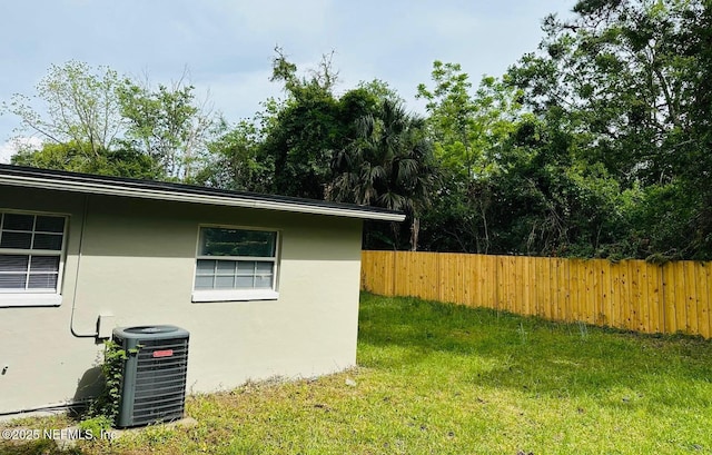 view of side of property with central AC, stucco siding, a yard, and fence