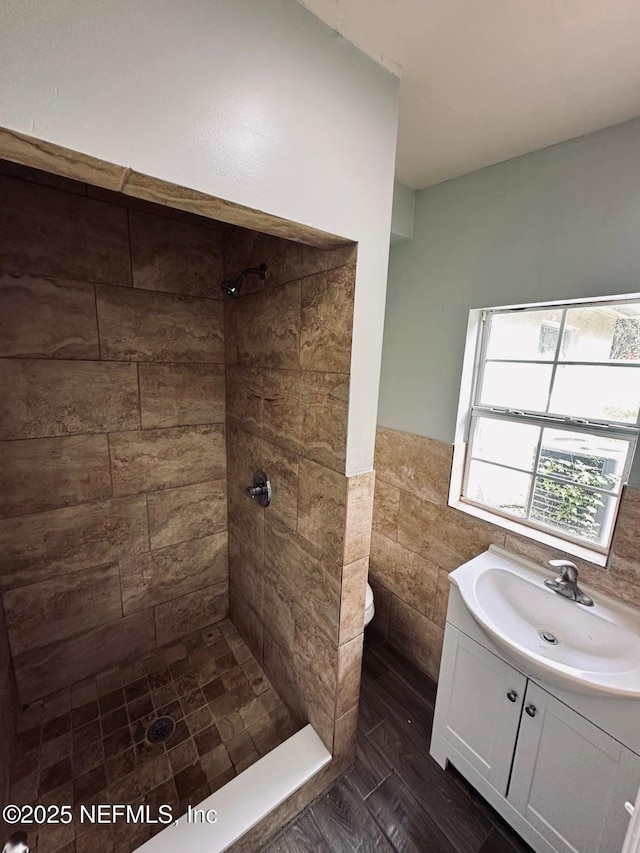 bathroom with tile walls, vanity, a wainscoted wall, toilet, and tiled shower