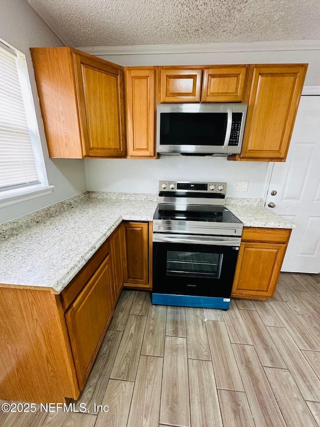 kitchen with brown cabinets, stainless steel appliances, a textured ceiling, and light wood finished floors
