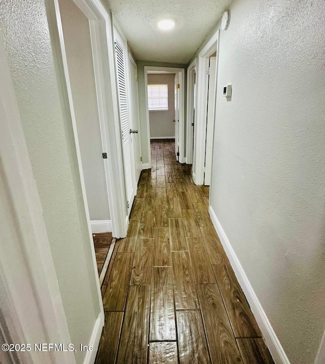 hallway with wood-type flooring, a textured ceiling, baseboards, and a textured wall