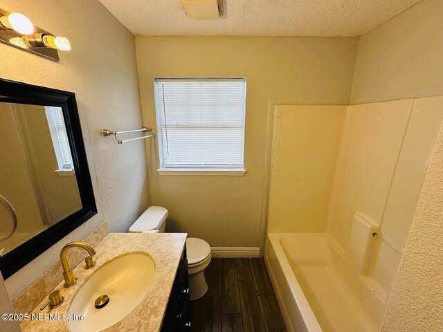 full bathroom with a textured ceiling, wood finished floors, vanity, baseboards, and toilet