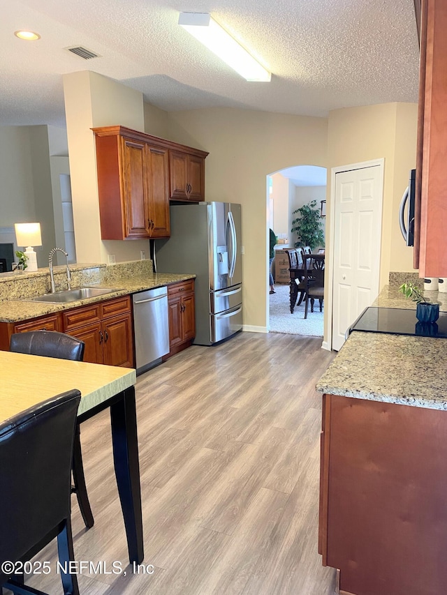 1831 Moss Creek Dr SW, Fleming Island, FL 32003 - kitchen featuring arched walkways, brown cabinets, a sink, light wood-style floors, and stainless steel appliances