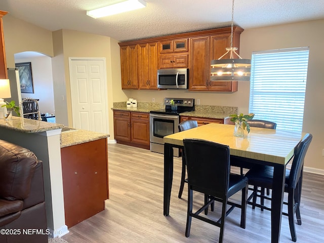 1831 Moss Creek Dr SW, Fleming Island, FL 32003 - kitchen with brown cabinetry, light wood-style floors, arched walkways, appliances with stainless steel finishes, and hanging light fixtures
