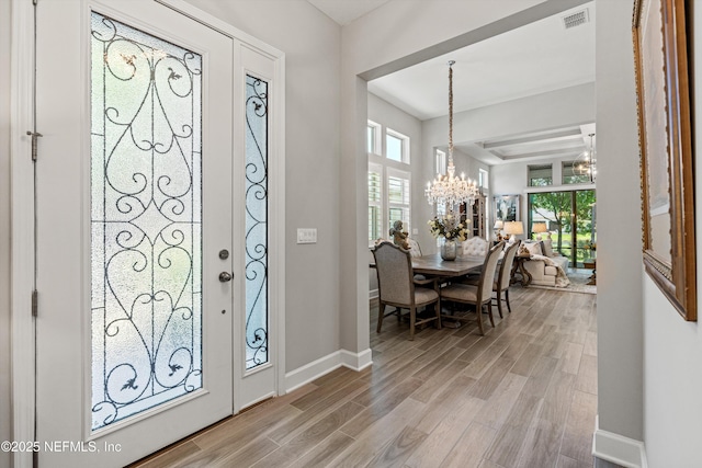 foyer entrance featuring an inviting chandelier, light wood-type flooring, visible vents, and baseboards