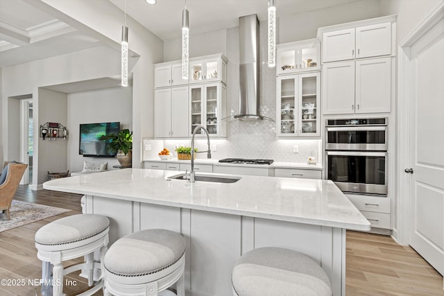 kitchen featuring stainless steel double oven, a sink, wall chimney exhaust hood, backsplash, and white cabinets