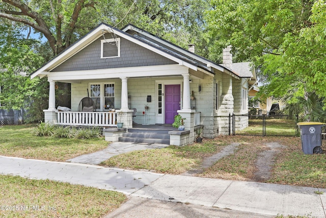 view of front facade featuring a porch, fence, a chimney, and a gate