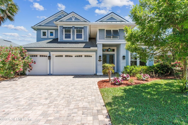view of front of house featuring roof with shingles, an attached garage, a front yard, decorative driveway, and french doors