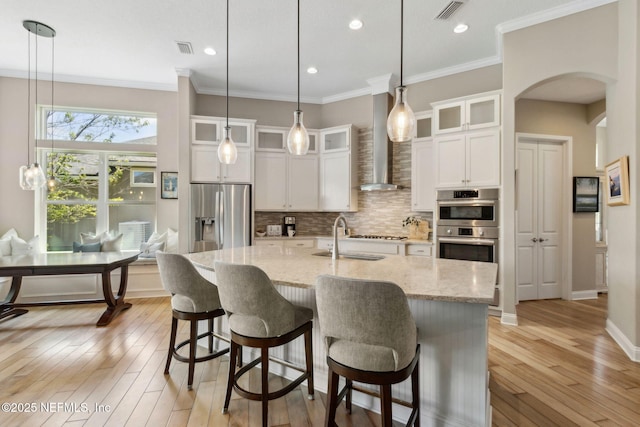 kitchen with visible vents, arched walkways, a sink, stainless steel appliances, and wall chimney exhaust hood