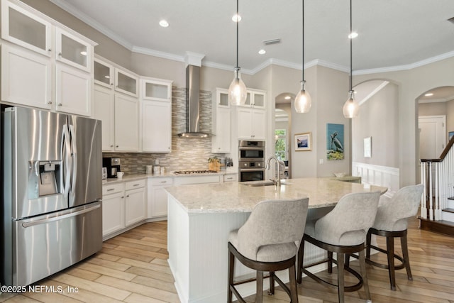 kitchen with wall chimney range hood, appliances with stainless steel finishes, a sink, light wood-style floors, and ornamental molding