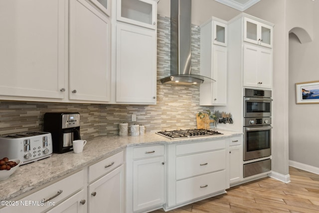 kitchen featuring wall chimney range hood, tasteful backsplash, a warming drawer, stainless steel appliances, and white cabinetry