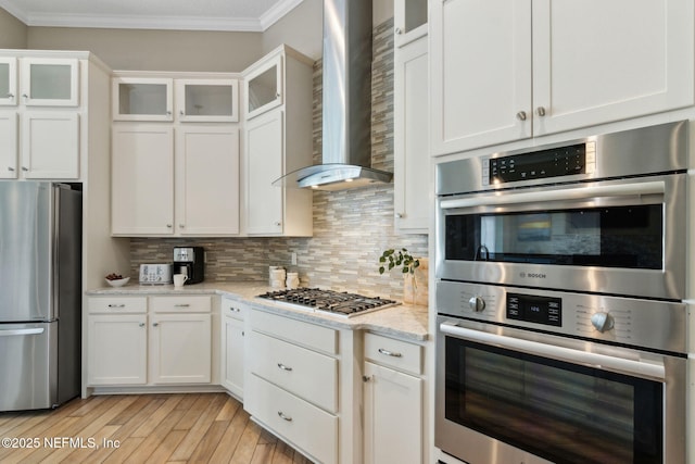 kitchen with wall chimney range hood, white cabinets, stainless steel appliances, tasteful backsplash, and ornamental molding
