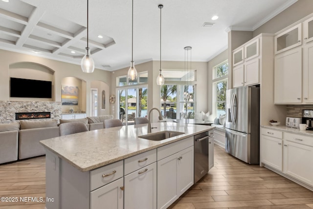 kitchen featuring a kitchen island with sink, a lit fireplace, recessed lighting, a sink, and appliances with stainless steel finishes