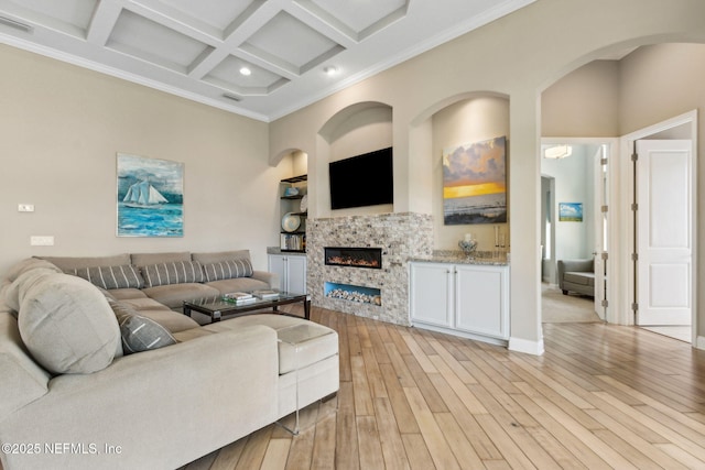 living room featuring crown molding, a glass covered fireplace, beamed ceiling, coffered ceiling, and light wood finished floors