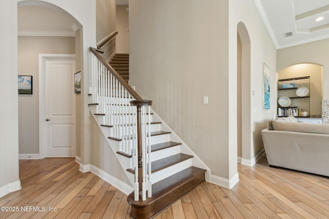 staircase featuring crown molding, arched walkways, baseboards, and hardwood / wood-style flooring
