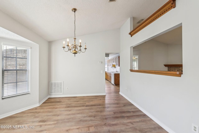 6085 Bermuda Dr, Fleming Island, FL 32003 - unfurnished dining area with a chandelier, a textured ceiling, wood finished floors, baseboards, and lofted ceiling