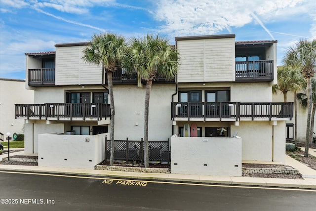 exterior space with stucco siding, a balcony, and fence