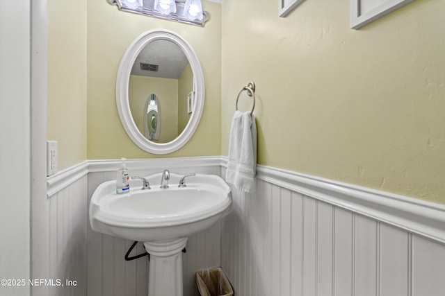 bathroom with visible vents, a sink, a decorative wall, and a wainscoted wall