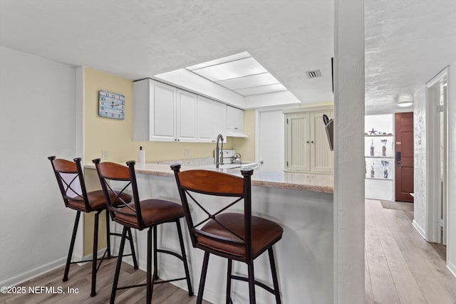 kitchen featuring a kitchen breakfast bar, a peninsula, light wood-style flooring, and visible vents